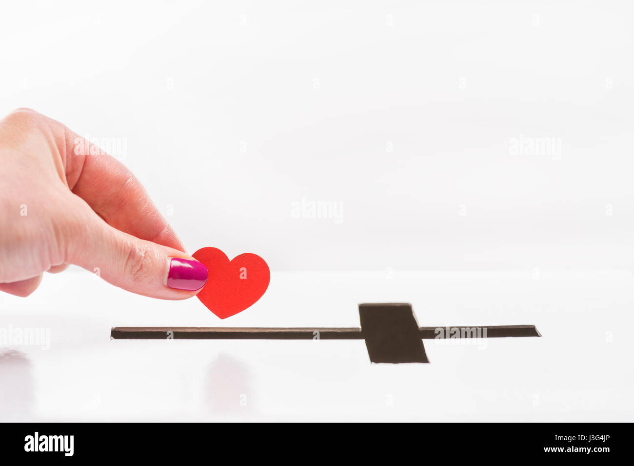 Close-up Teilansicht des Woman einfügen Rot Herz Symbol in Loch für Spenden in Form eines Kreuzes, Spende und Glaubens-Konzept Stockfoto
