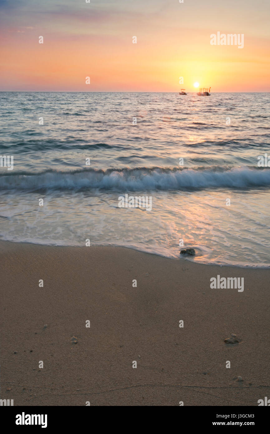 Sunrise Landschaft der Ozean mit Abstand Boote, Wellen und Felsen am Strand Stockfoto