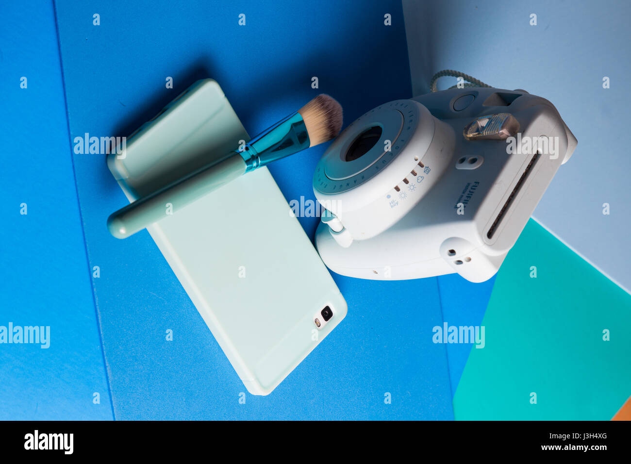 Ihr Leben auf Blautöne: Stillleben mit einer Sofortbild-Kamera, Smartphone und einem Make-up-Pinsel in eine mehrfarbig Blautöne platziert Stockfoto