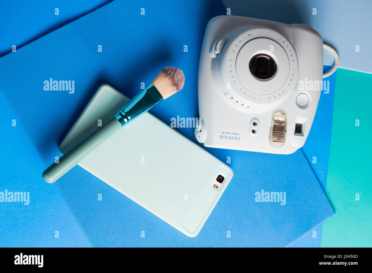 Ihr Leben auf Blautöne: Stillleben mit einer Sofortbild-Kamera, Smartphone und einem Make-up-Pinsel in eine mehrfarbig Blautöne platziert Stockfoto