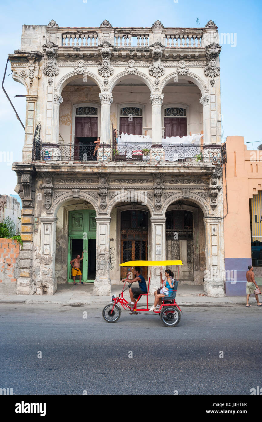 Havanna - Juni 2011: Fahrrad Taxi trägt einen Passagier vor bröckelnden Kolonialarchitektur in einer ruhigen Straße im Centro. Stockfoto