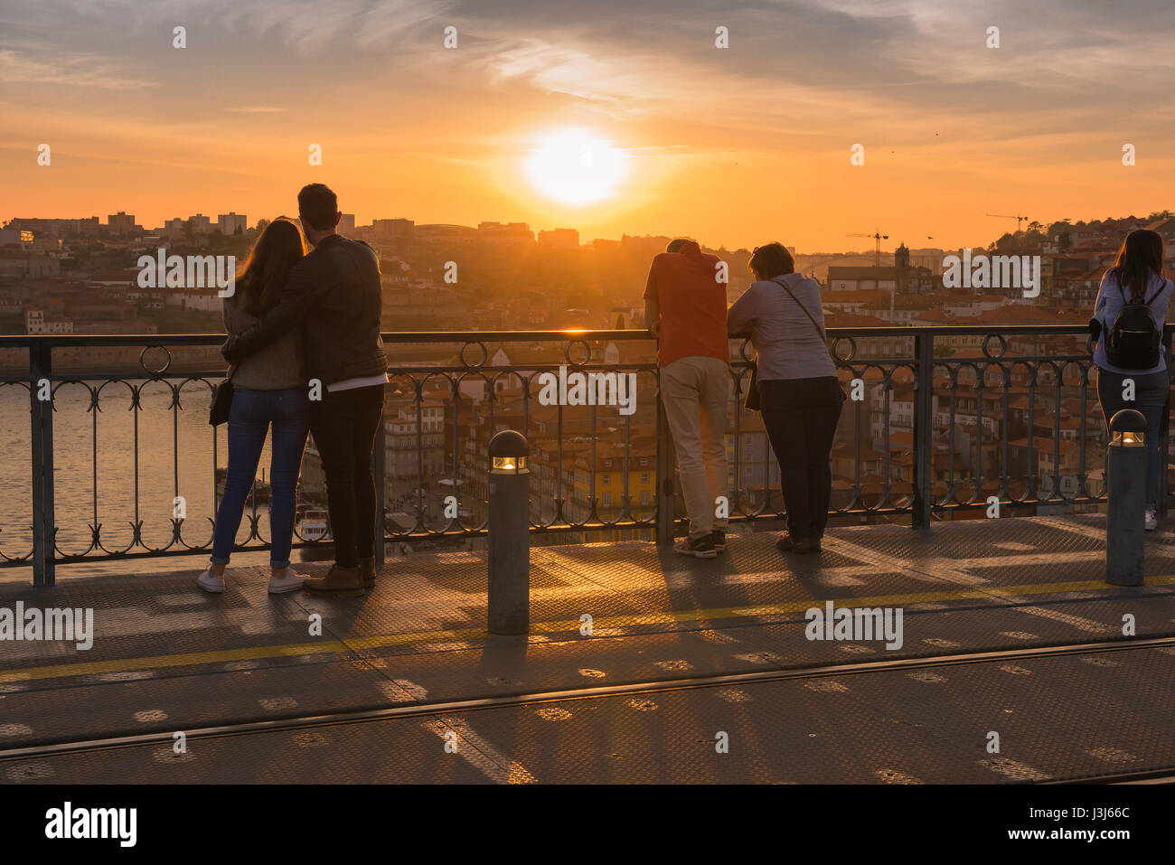 Romantische Reise, Rückansicht eines jungen Paares und eines Paares mittleren Alters, die nebeneinander stehen und einen Sonnenuntergang über einer europäischen Stadt, Europa, beobachten Stockfoto
