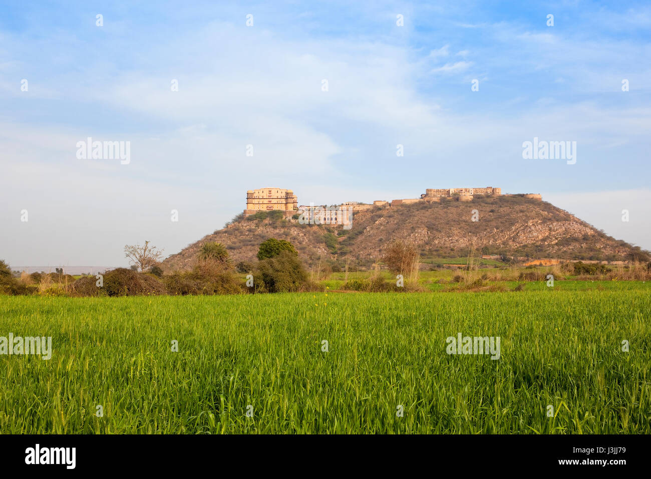 Das schöne Tijara Fort Hotel in Nordindien auf einem sandigen Hügel Weizenfelder unter einem blauen bewölkten Himmel im Frühling Stockfoto