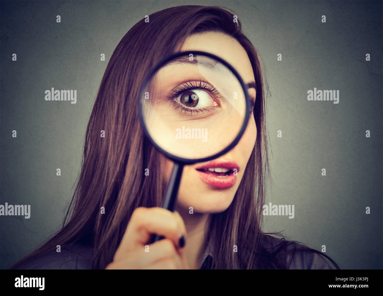 Neugierige Frau, die durch ein Vergrößerungsglas Stockfoto