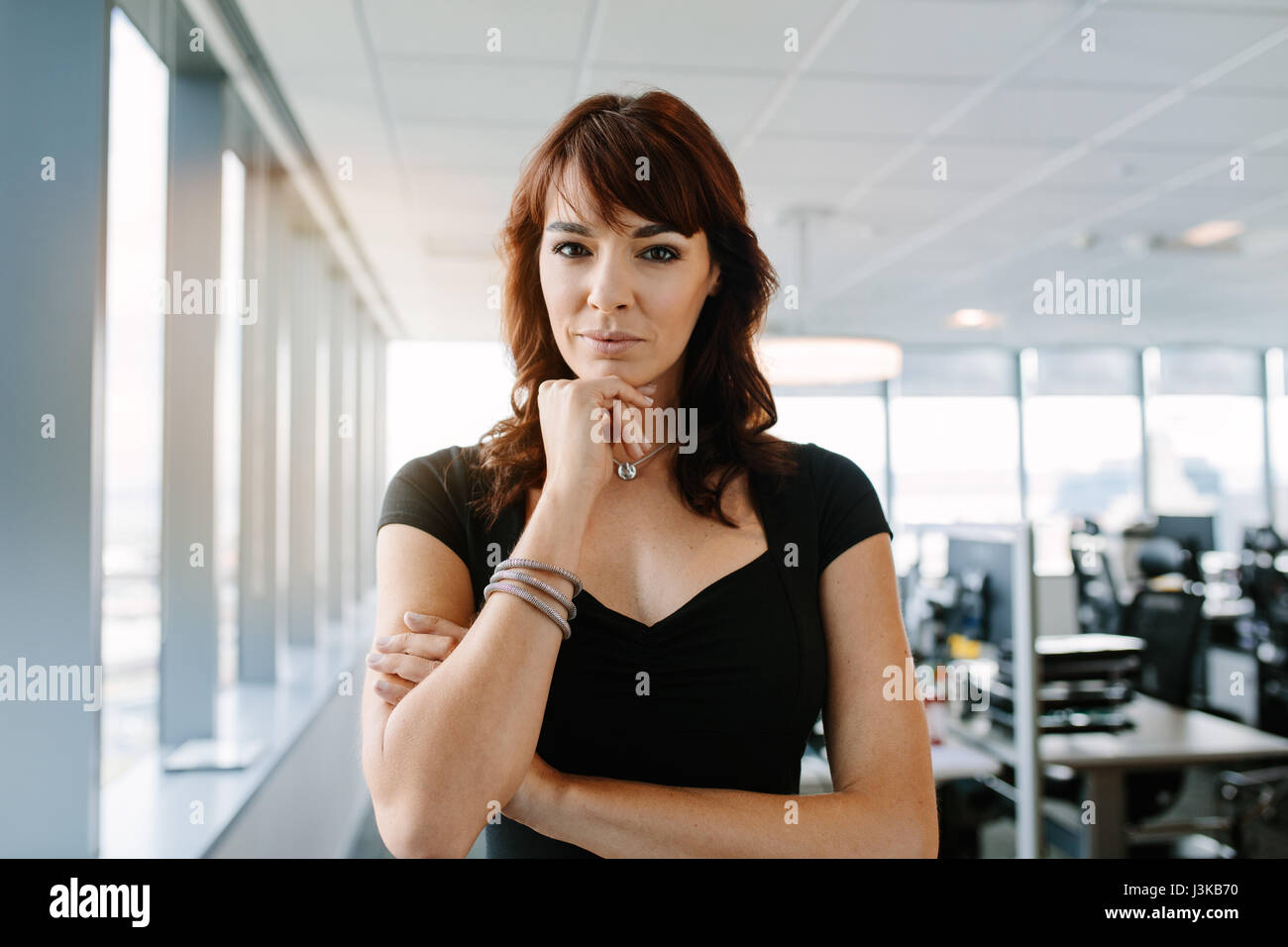 Porträt von schöne und selbstbewusste Geschäftsfrau, stehend im Büro mit der Hand am Kinn. Kaukasische weibliche Führungskraft Blick in die Kamera. Stockfoto