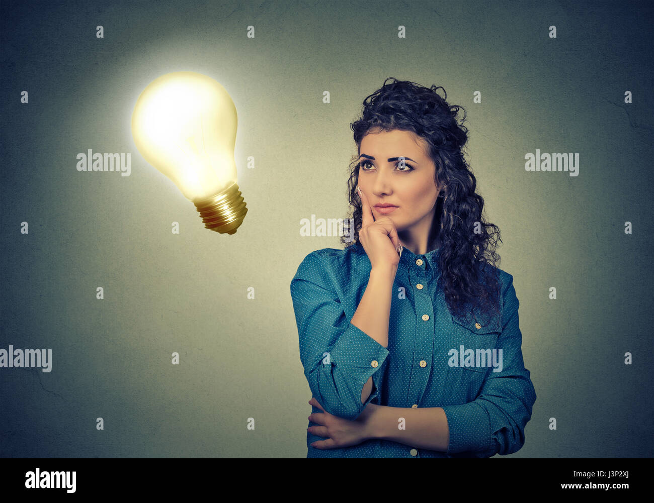 Closeup schönes Mädchen denkt blickte zu helle Glühbirne auf graue Wand Hintergrund isoliert. Konzept, Idee, Bildung und Menschen. Gesichtsausdruck Stockfoto