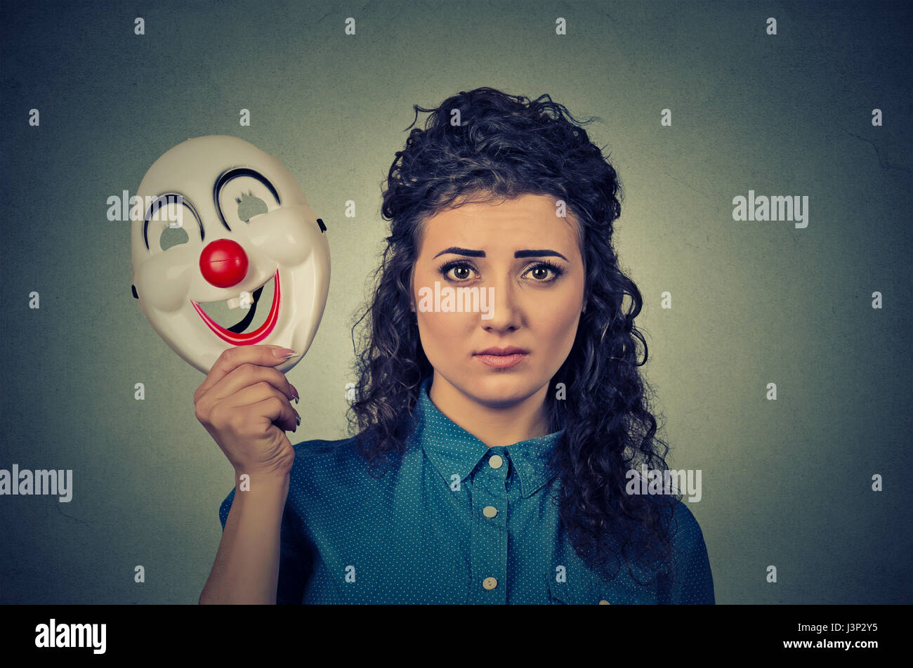 Porträt-junge aufgeregt besorgt Frau mit traurigen Ausdruck hält eine Clownsmaske mit dem Ausdruck ihrer Fröhlichkeit Glück auf graue Wand Hintergrund isoliert Stockfoto