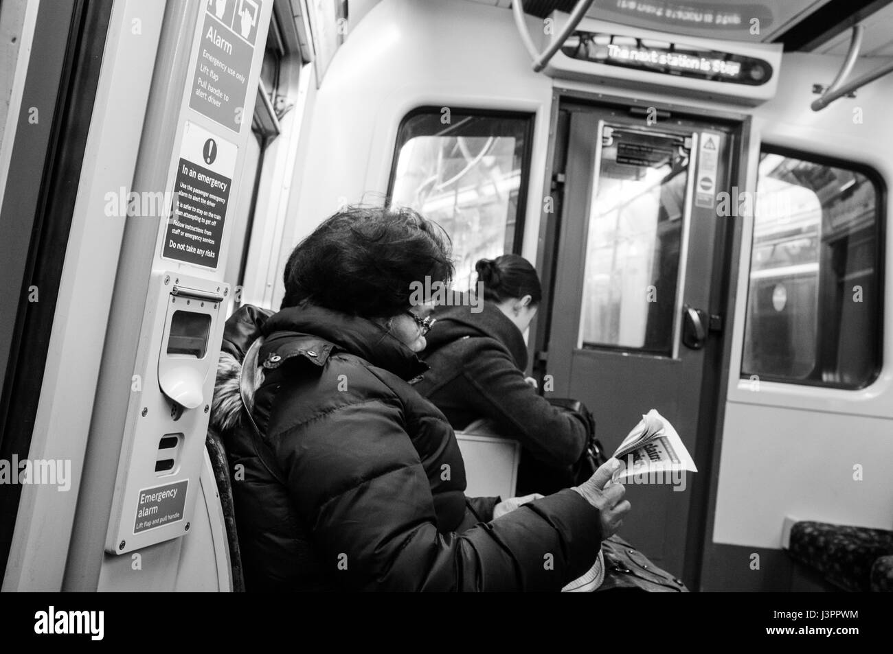 Frau liest Zeitung Hammersmith & City Line-Zug auf der Londoner U-Bahn. Stockfoto