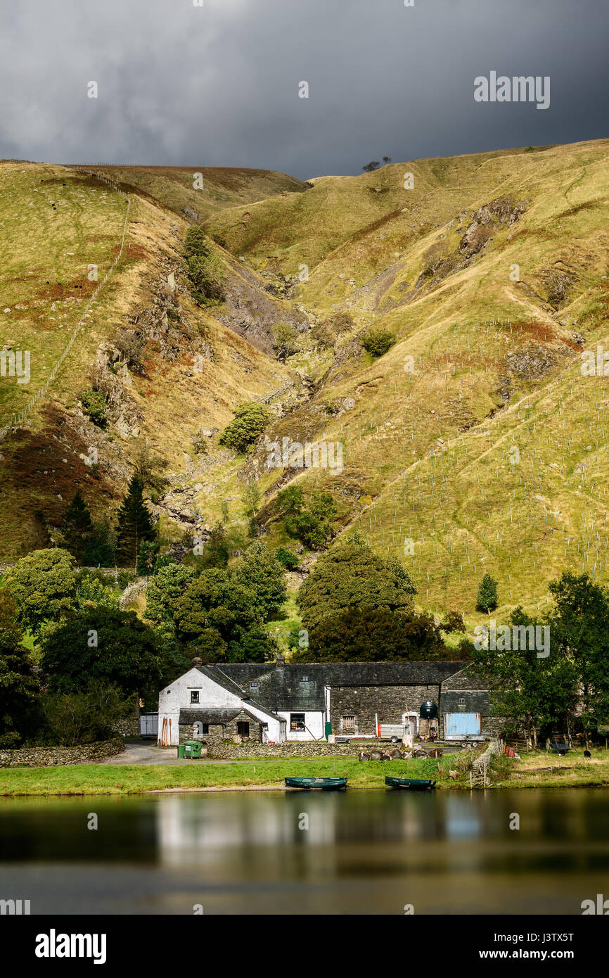 Eine funktionierende Cumbrian Bergbauernhof spiegelt sich in dem ruhigen Wasser an der Basis eine englische fiel unter einem düsteren Himmel. Stockfoto