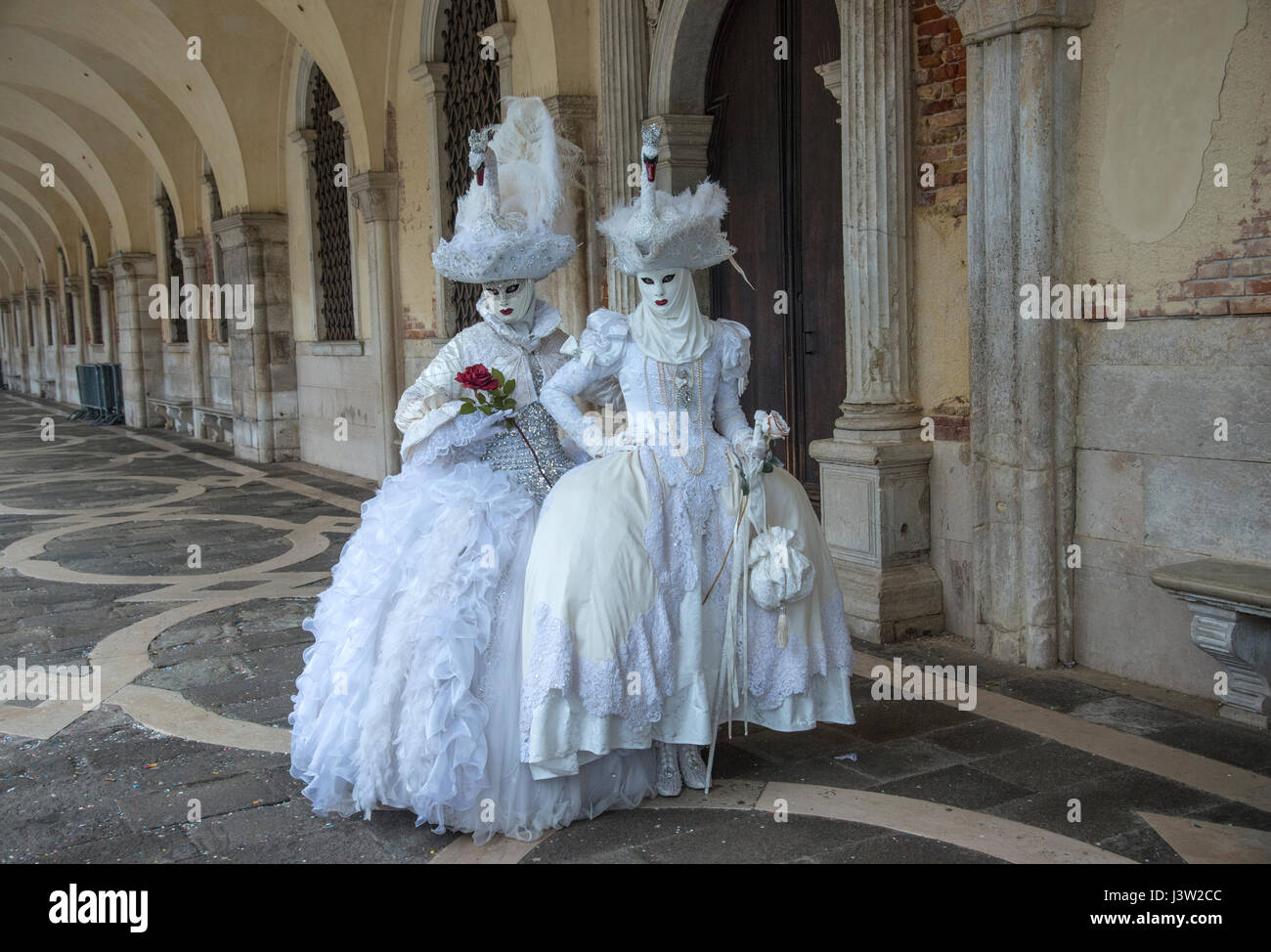 Bild von zwei Personen in komplementären kunstvollen Kostümen entlang des Dogenpalastes während des Karnevalfestes in Venedig, Italien. Stockfoto