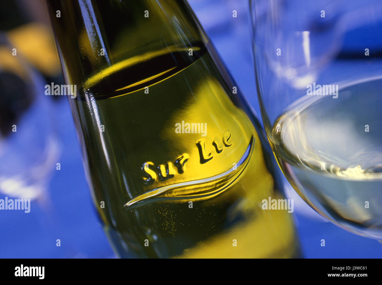 Blick auf Muscadet Sur Lie auf Weinflasche mit Reliefetikett, das „Sur Lie“ bezeichnet, und gegossenes Glas trockenen französischen Weißweins auf einem blauen Alfresco-Tisch Stockfoto
