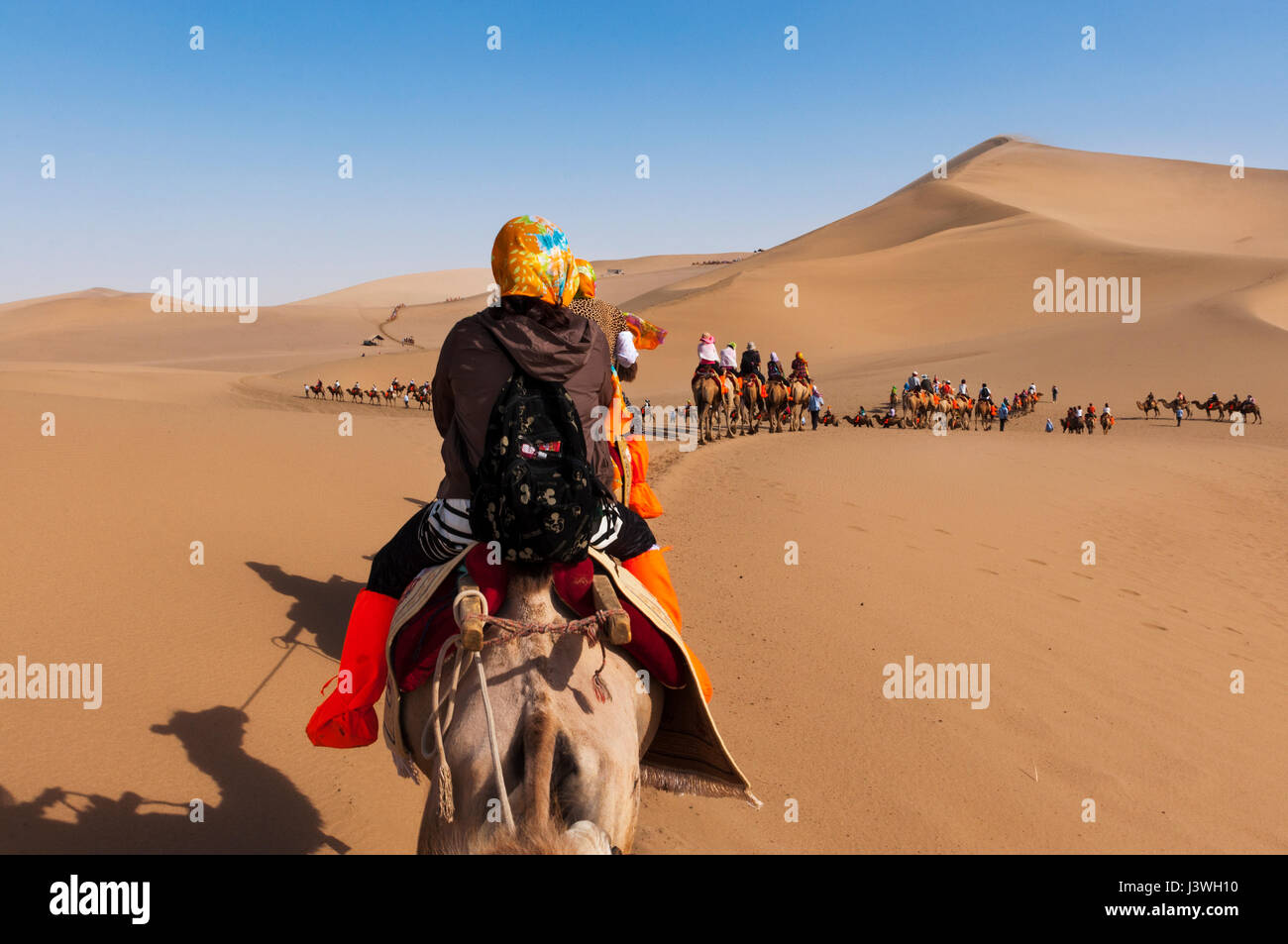 Dunhuang, China - 8. August 2012: Touristen auf einem Kamel-Karawane in den Dünen rund um die Stadt Dunhuang in der alten Seidenstraße in China. Stockfoto