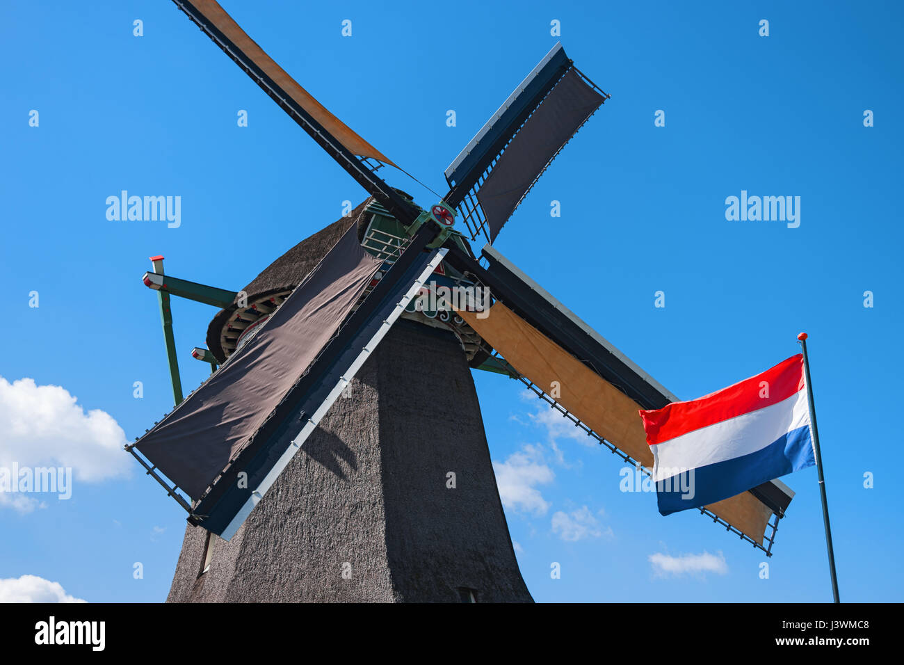 Alte Windmühle und wehende Flagge, Zaanse Schans, Niederlande. Typische holländische Mühle. Landschaft im ländlichen Raum. Symbol der Niederlande Stockfoto