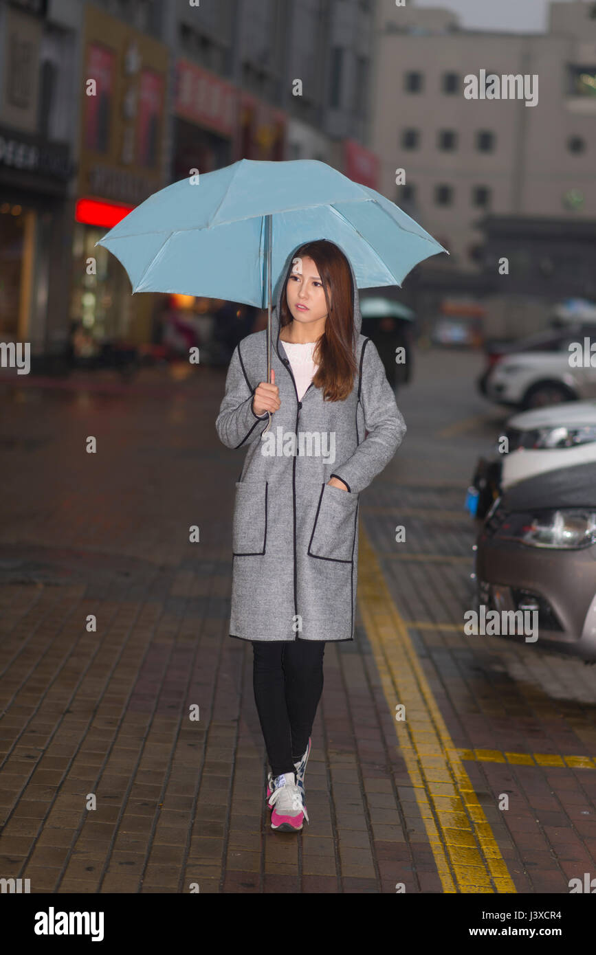 Frau ist in der Nacht Spaziergang im Regen mit blauen Schirm Stockfoto