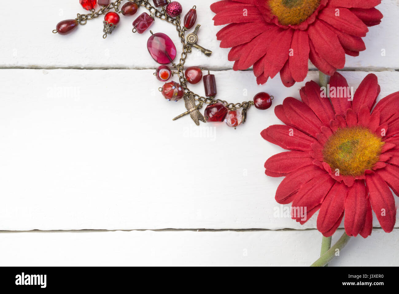 Rote Chrysanthemen / Daisy Blumen auf weißem Holz Hintergrund hautnah mit rotem Glas und gold Bettelarmband - Raum für Text Stockfoto