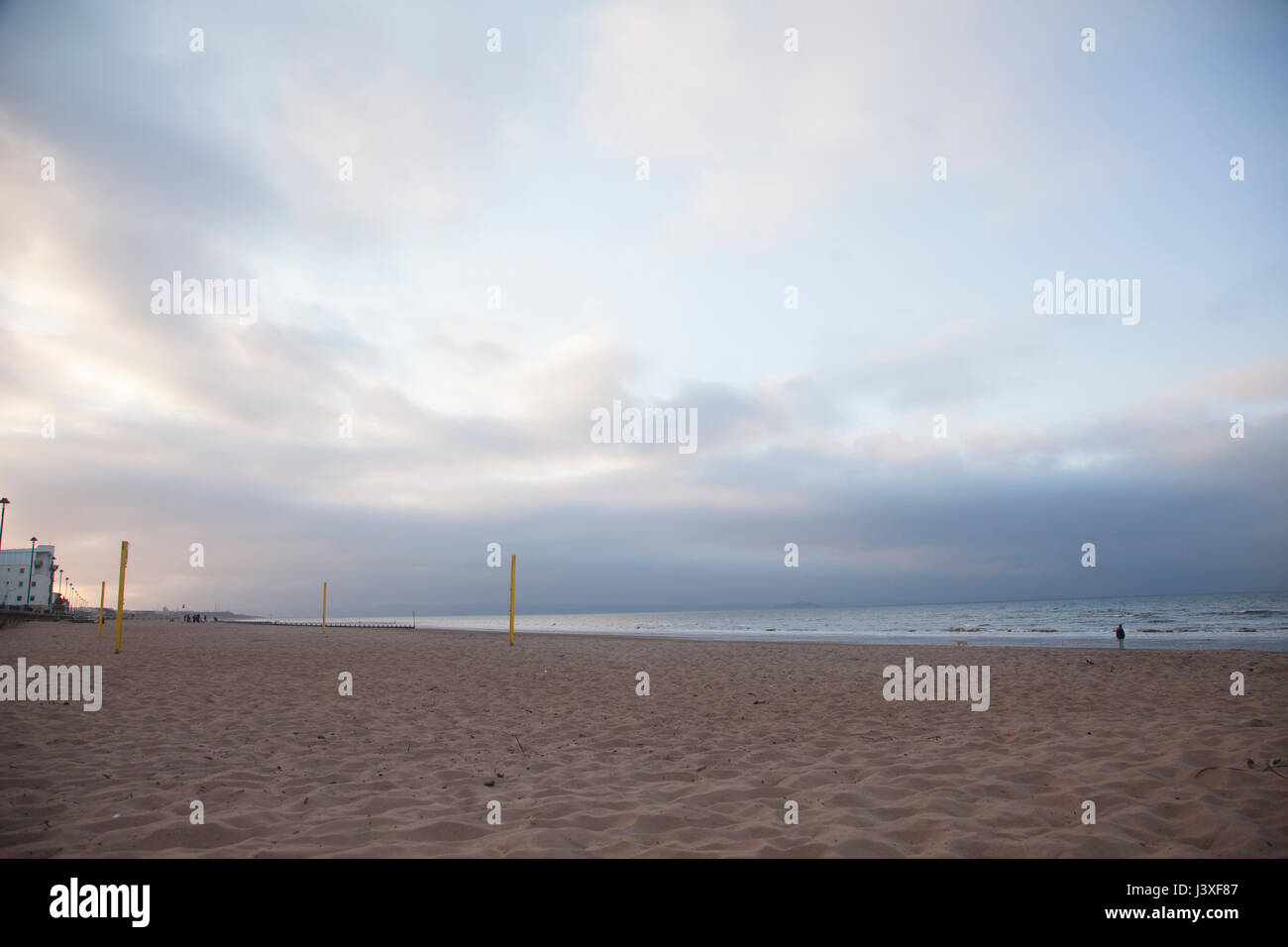 Mann mit dem Hund zu Fuß in Richtung Meer im Sonnenuntergang. Portobello Beach in Edinburgh, die Hauptstadt von Schottland, UK. Stockfoto