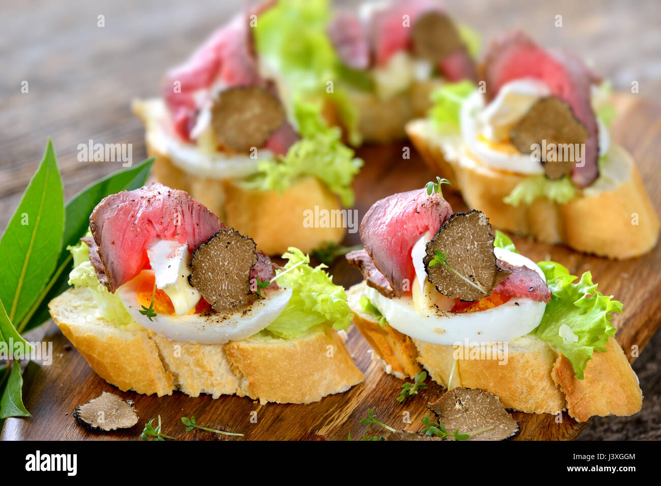 Canapes mit Roastbeef, schwarze Herbst Trüffel, französischer Brie Käse auf eine Scheibe Ei auf Baguette mit einem Blatt Salat Stockfoto