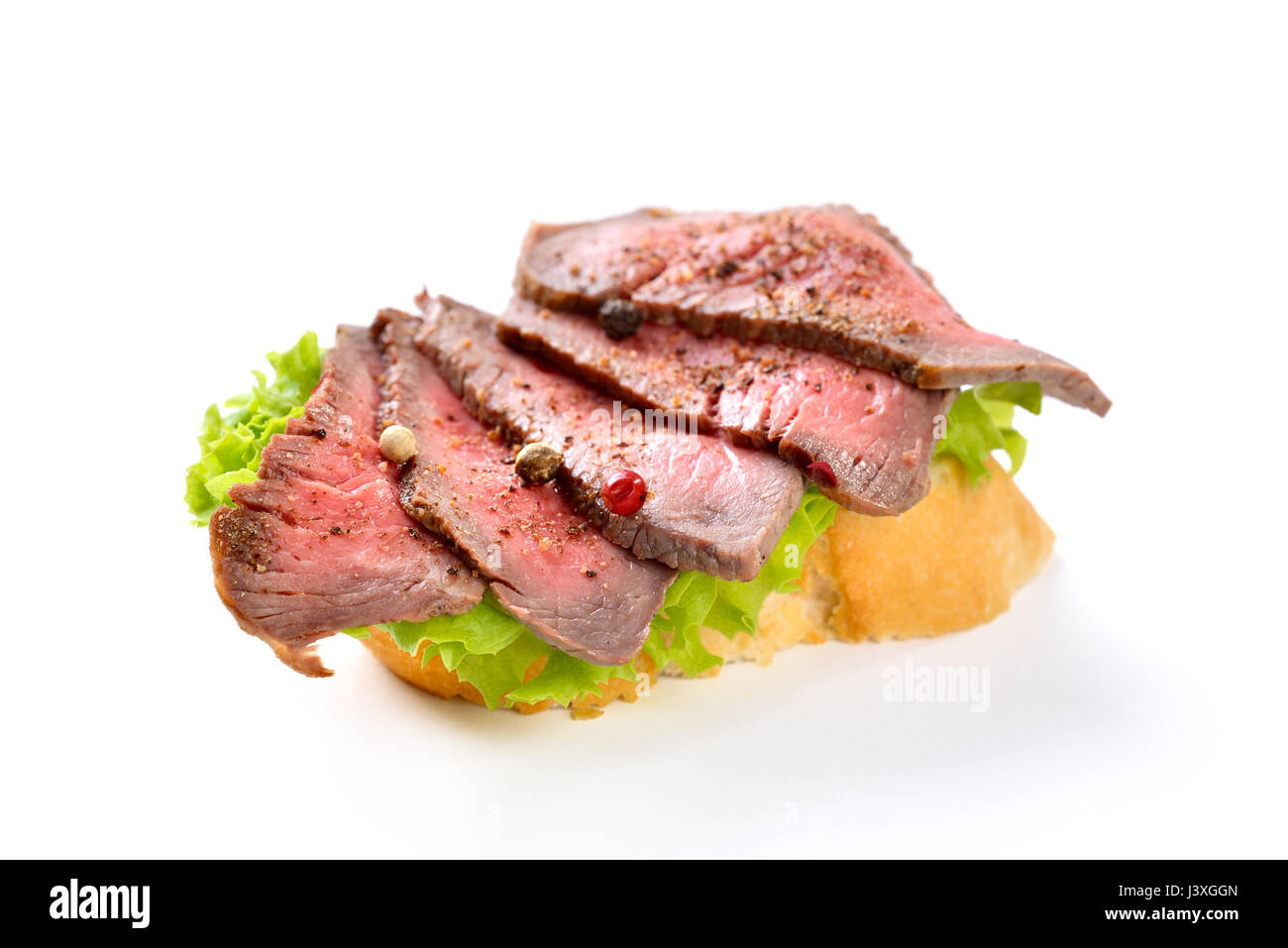 Gebratenes Rinderfilet mit Pfeffer auf einer Scheibe Baguette mit einem Blatt Salat Stockfoto