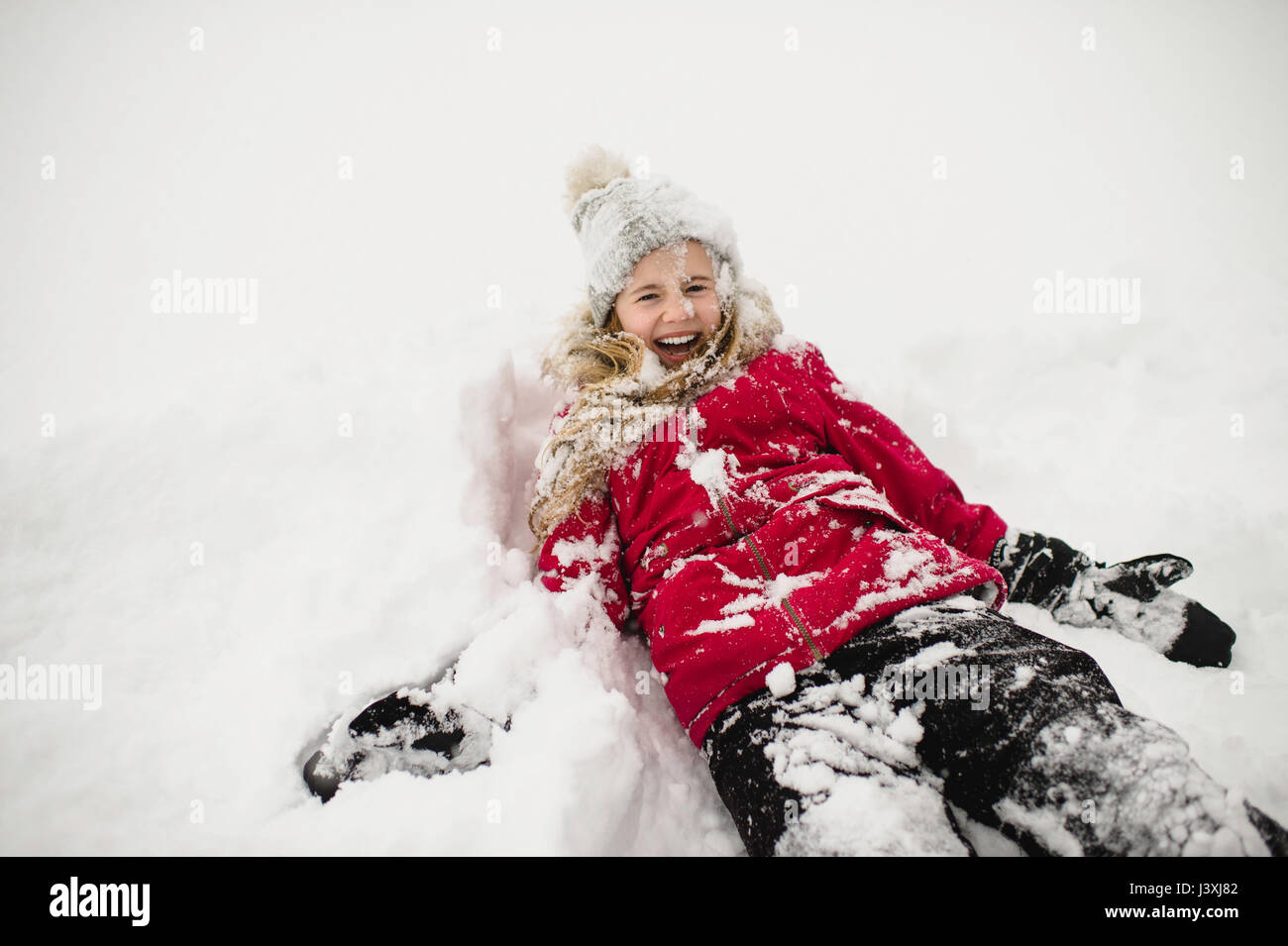 Lächelndes Mädchen liegend zurück und bedeckt im Schnee Stockfoto