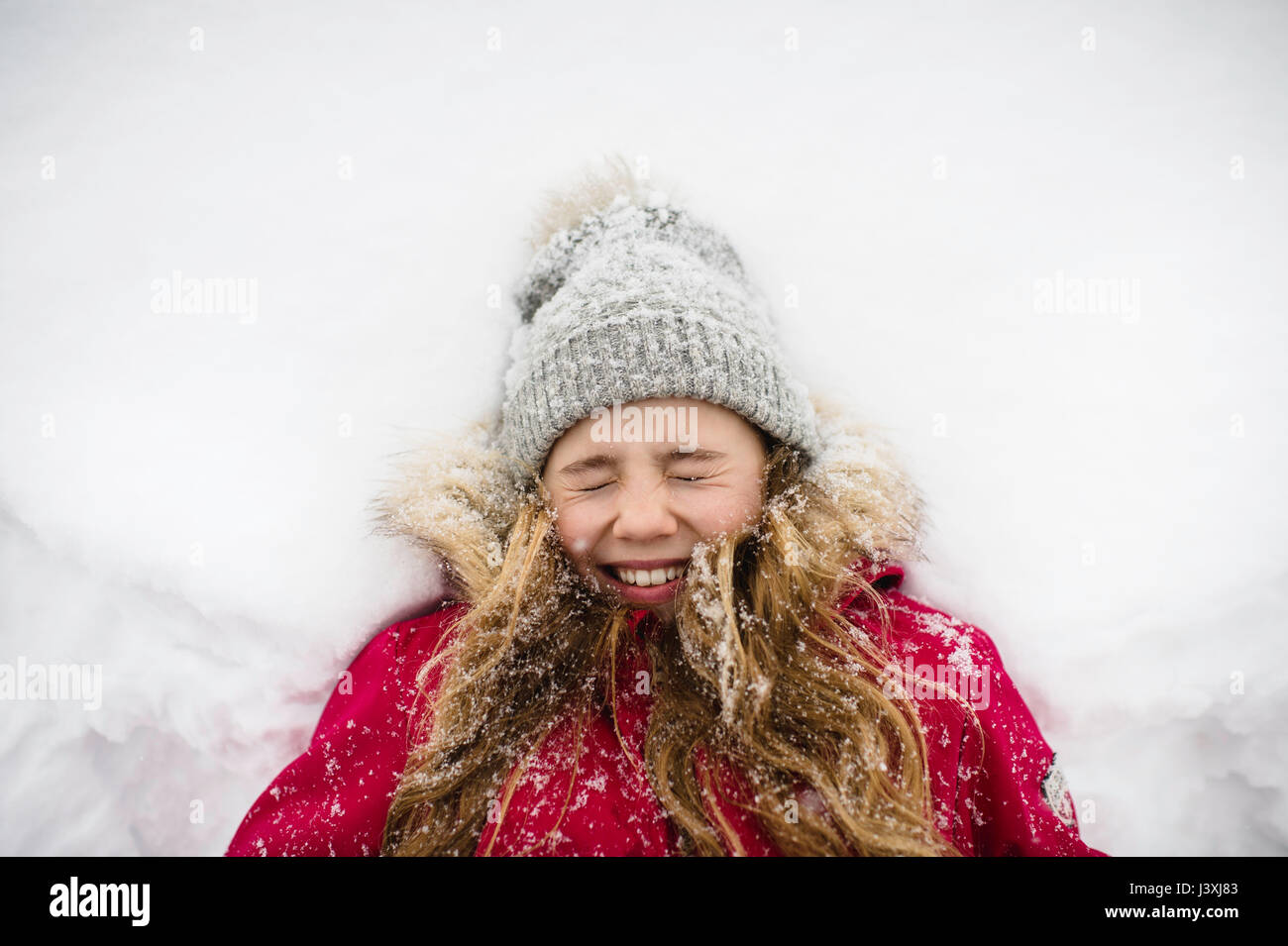 Mädchen auf Rücken im Schnee liegend mit Augen geschlossen Stockfoto