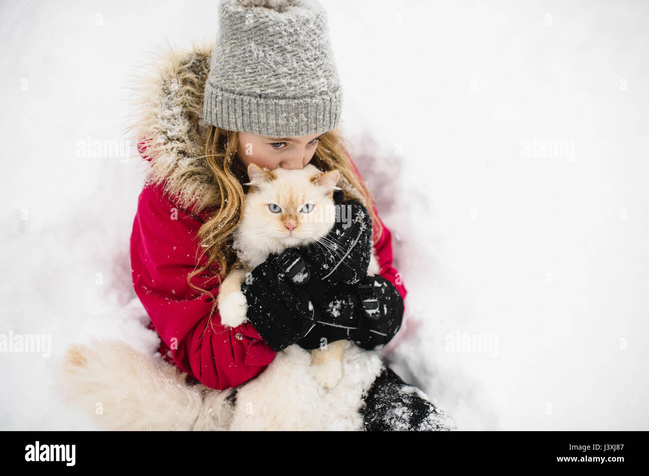 Portrait von Green Eyed white cat umarmte von Mädchen im Schnee Stockfoto