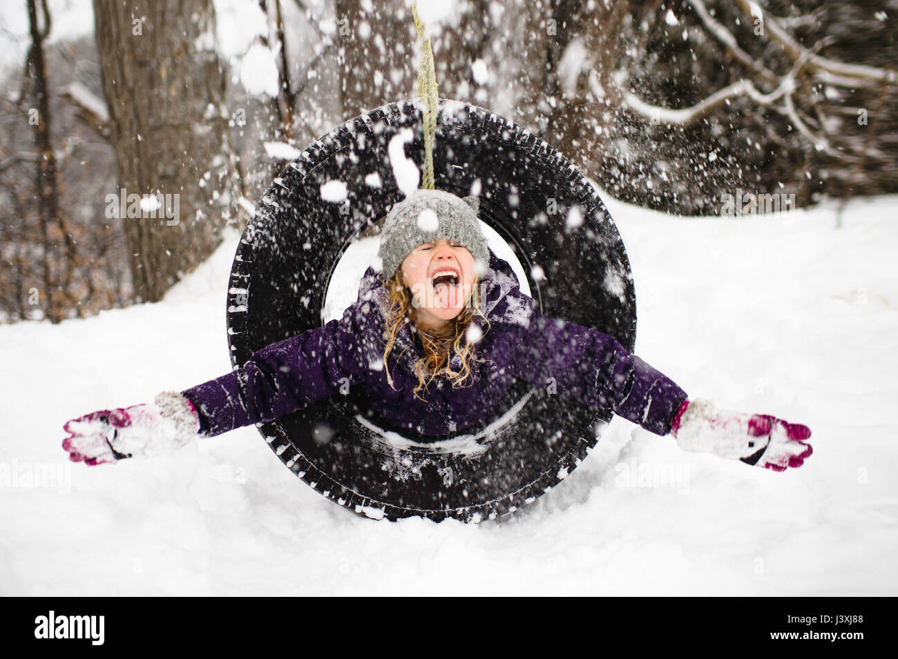 Mädchen spielen im Schnee auf Reifenschaukel Stockfoto