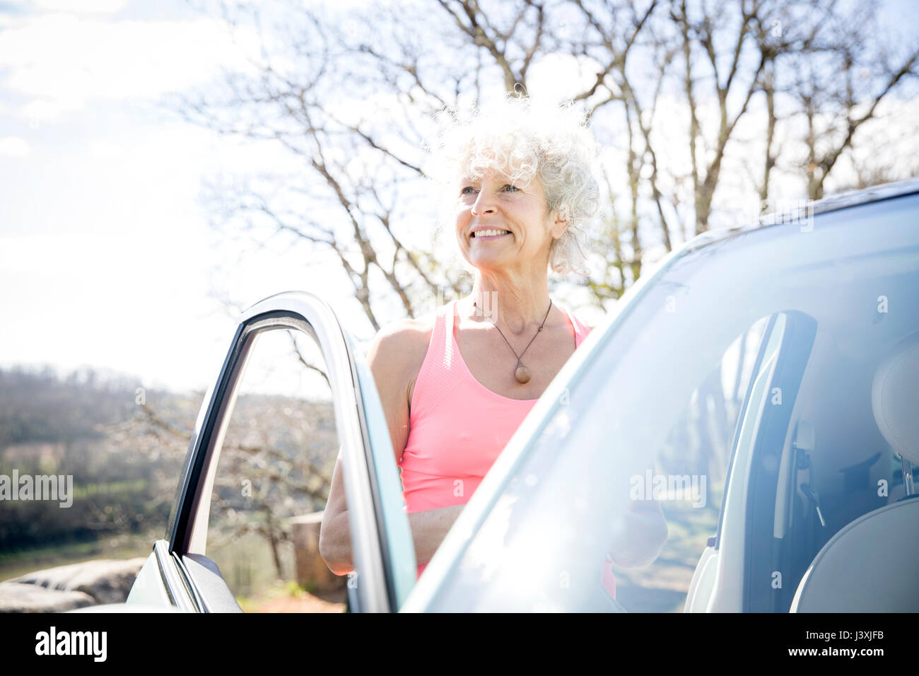 Reife Frau mit dem grauen Haar steht mit dem Auto auf die ländliche Straße Stockfoto