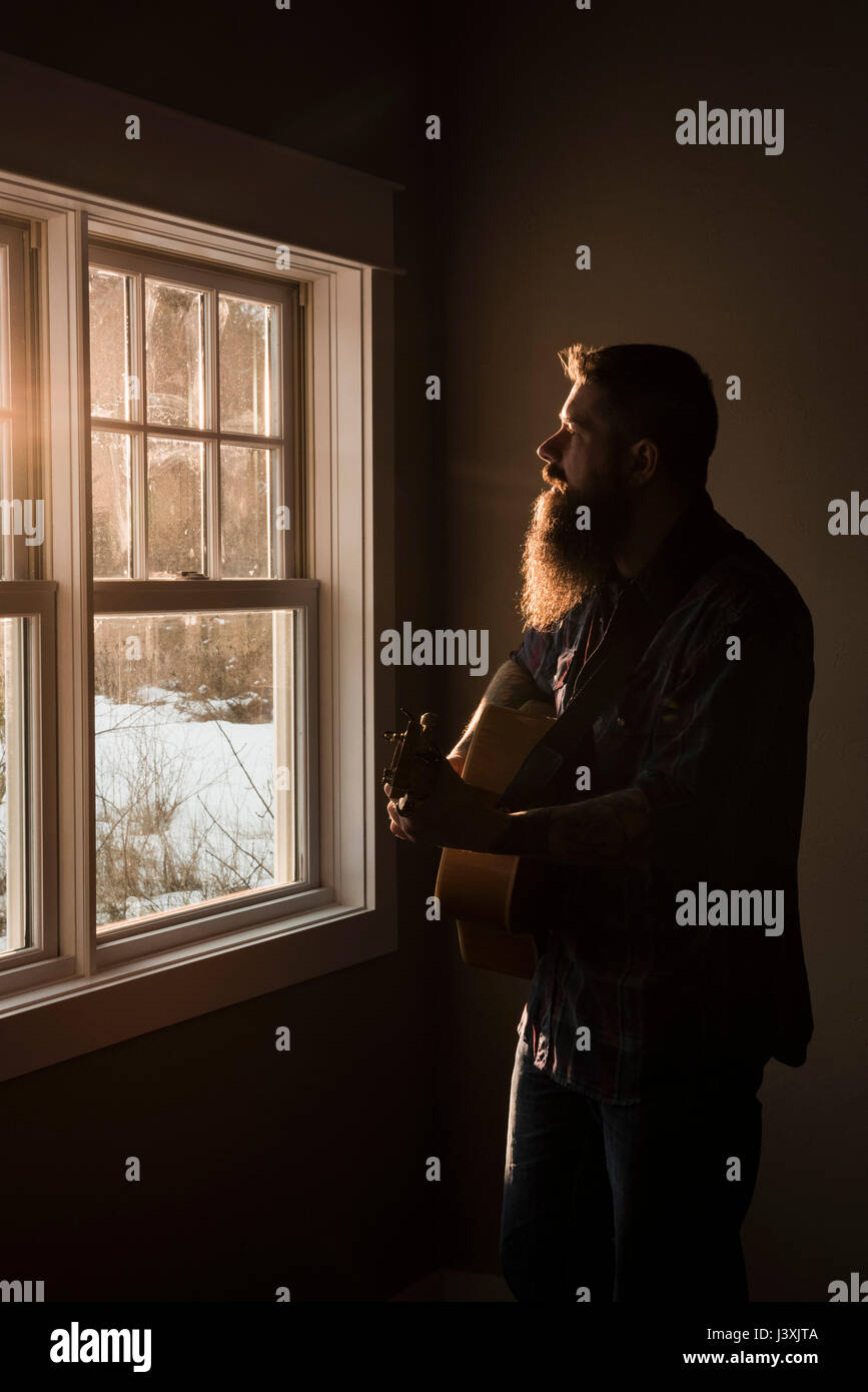 Mann Gitarre spielen neben Fenster Stockfoto
