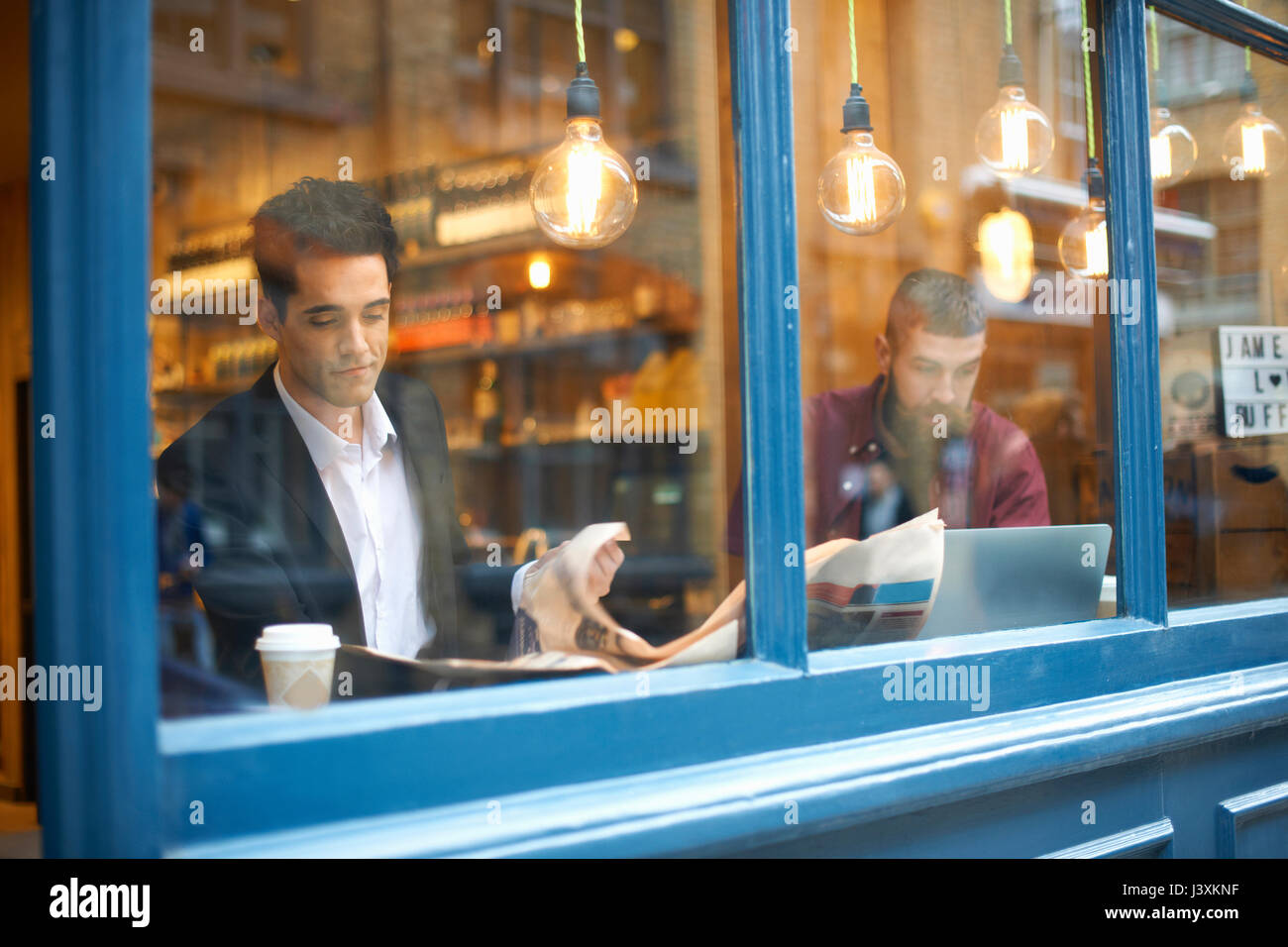 Fenster mit Blick auf die Unternehmer lesen Zeitung und mit Laptop im Cafe Stockfoto