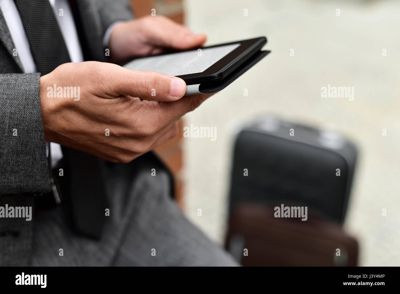 Nahaufnahme eines jungen kaukasischen Geschäftsmann in einem grauen Anzug mit einem Tablet im Freien, neben seinem Gepäck Stockfoto