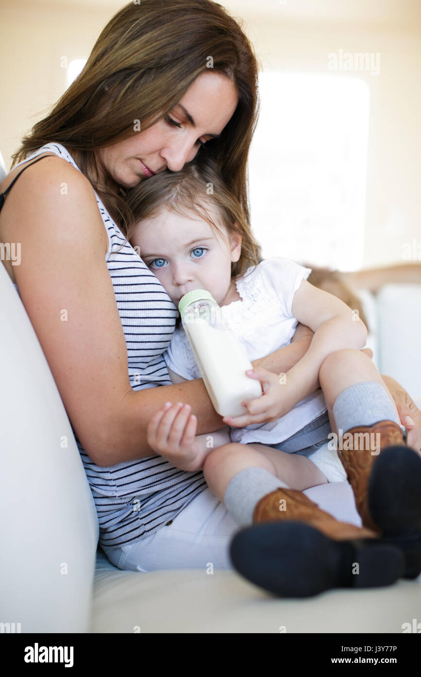 Weiblichen Kleinkind auf Mutters Schoß aus Babyflasche trinken Stockfoto
