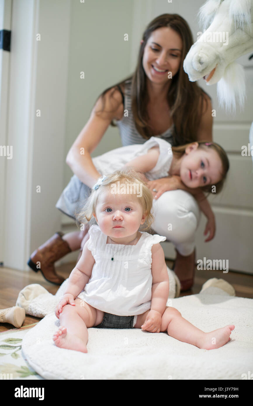 Porträt von Babymädchen sitzen auf Boden mit Mutter und Schwester hinter Stockfoto