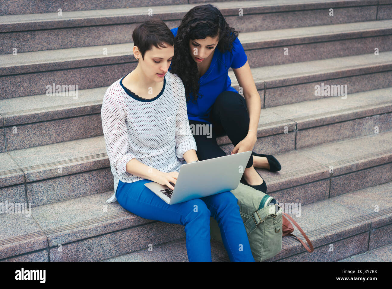Zwei Frauen sitzen auf Stufen, Blick auf laptop Stockfoto
