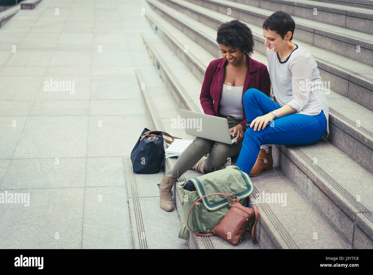 Zwei Frauen sitzen auf Stufen, Blick auf laptop Stockfoto