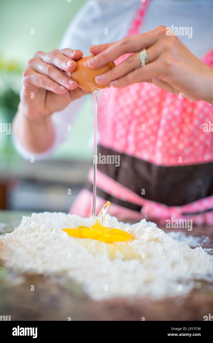 Reife Frau knacken Ei auf Mehl, Mittelteil Stockfoto