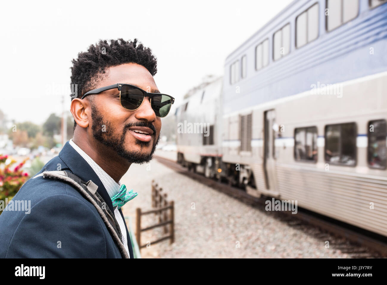 Junger Geschäftsmann in Fliege beobachten Zug ankommen am Bahnsteig Stockfoto