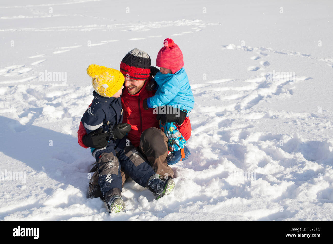 Vater sitzen im Schnee, umarmen zwei Söhne Stockfoto