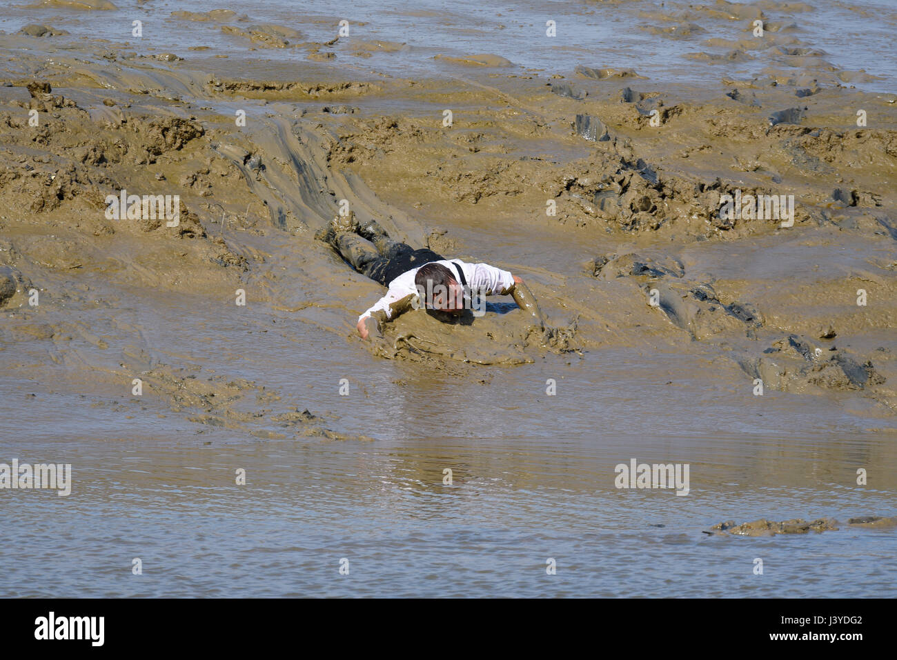 Richard Emerson, Sieger des Mad Maldon Mud Race, rutscht über den Fluss Chelmer in Essex, Großbritannien Stockfoto