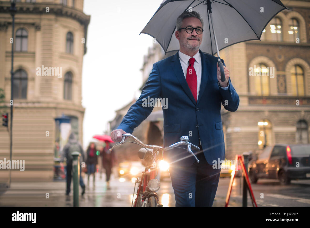 Gut aussehender Mann auf der Straße unter dem Regen. Er hält sein Fahrrad und schützen sich mit einem Regenschirm. Stockfoto