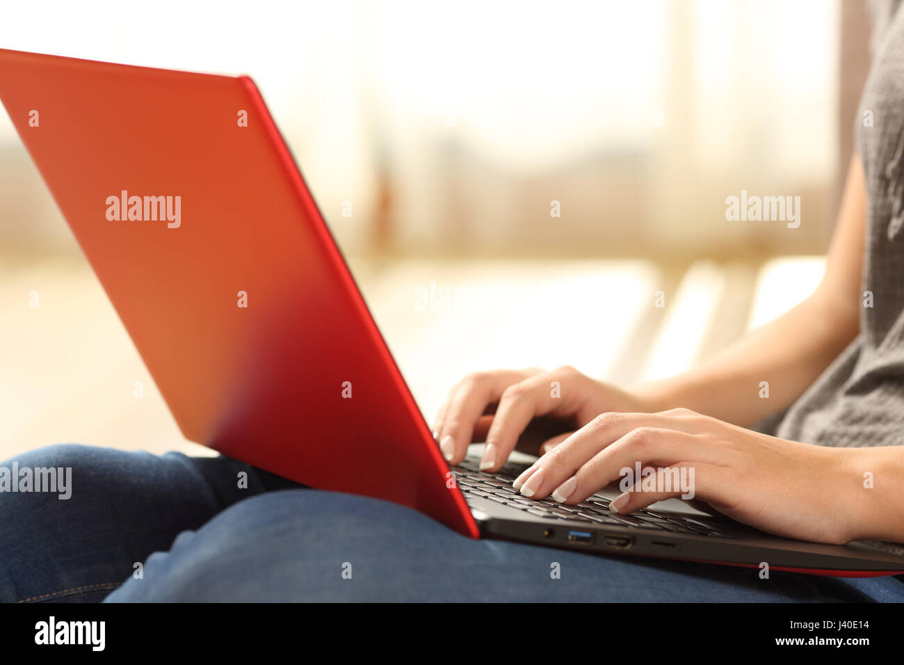 Hände eines einzigen Mädchens eine rote Laptop sitzen auf dem Boden des Wohnzimmers zu Hause mit einem Fenster und warmes Licht im Hintergrund e-Mail eintippen Stockfoto
