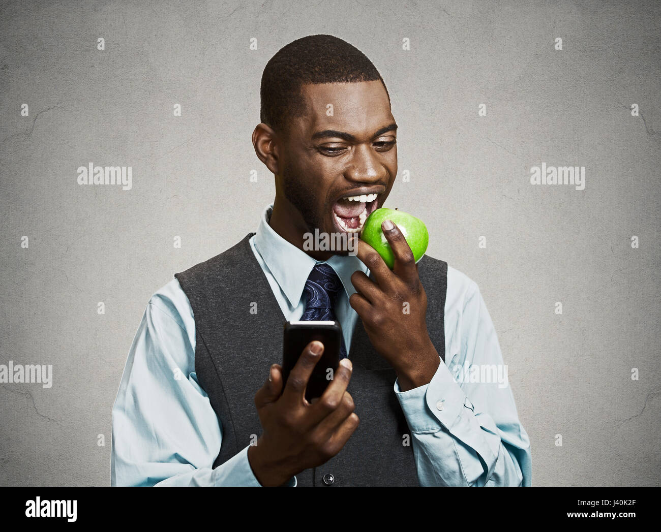 Closeup Portrait ernsthafte Business-Mann, Deal Maker lesen schlechte Nachrichten auf intelligente, Handy halten, Essen grüner Apfel isoliert schwarz grau hinterlegt. Stockfoto