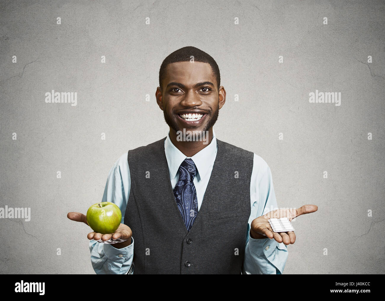 Closeup Portrait Fit glücklich executive Jüngling Holding grünen frischen Apfel in einer Hand, Pillen, Vitamine in einem anderen, versuchen zu entscheiden, welche Wahl ist die Stockfoto