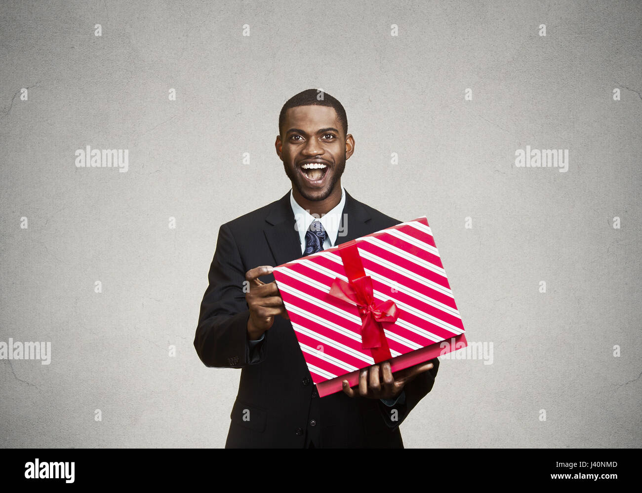 Closeup Portrait junge glücklich aufgeregt Mann rote Geschenkbox, zufrieden, dankbar, mit was er bekommen, isoliert schwarzen, grauen Hintergrund zu öffnen. Positiven huma Stockfoto