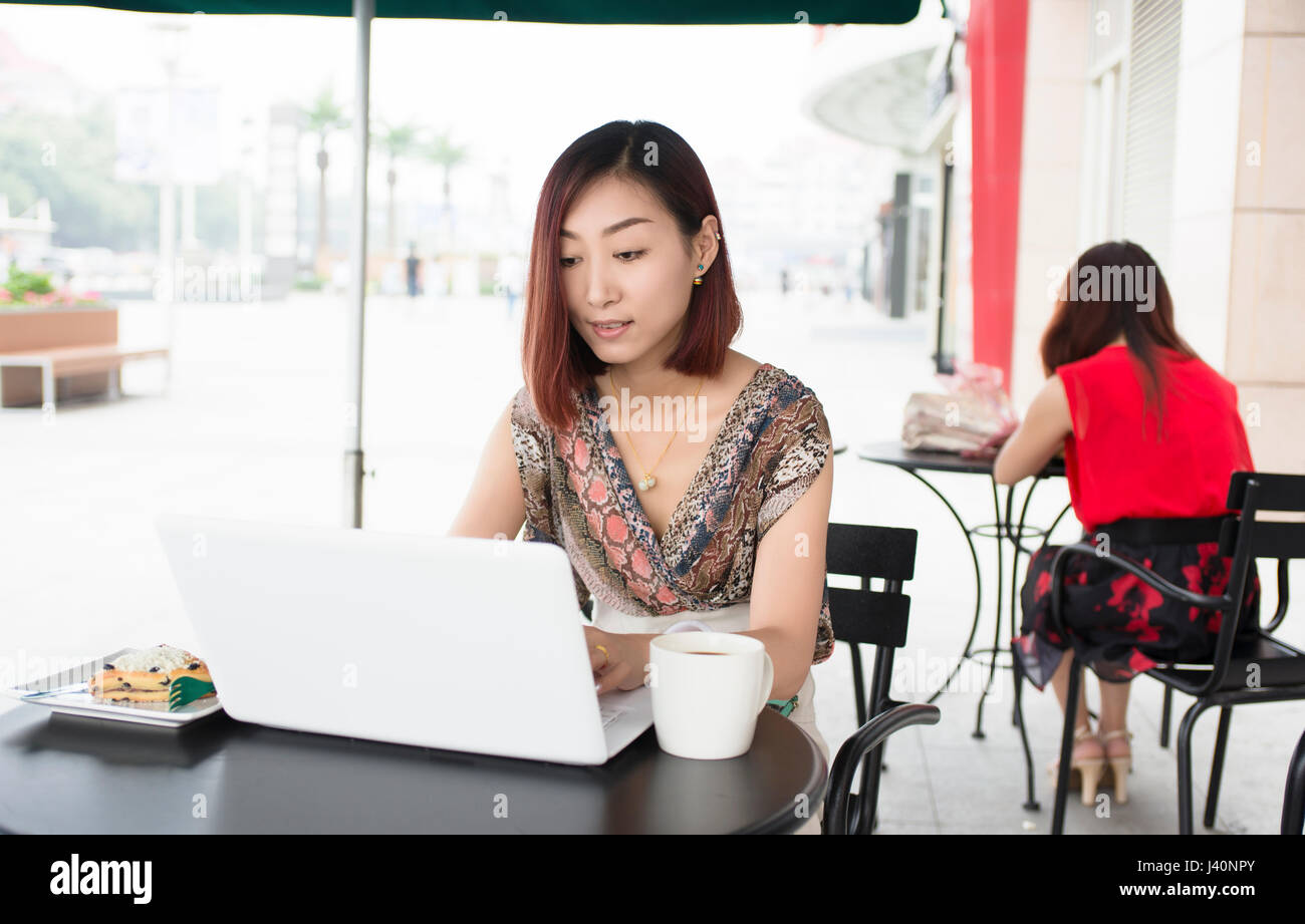Junge Frau mit ihrem Laptop im Café im Freien sitzen Stockfoto