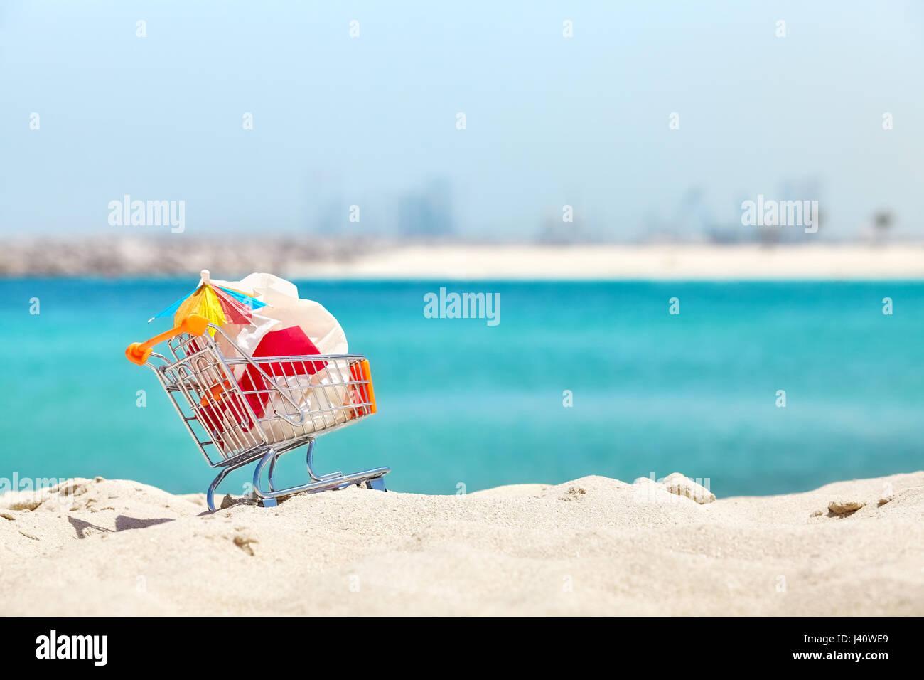 Miniatur-Einkaufswagen mit Plastiktüte und cocktail Regenschirm von Tourist an einem tropischen Strand, Umweltverschmutzung Konzept Bild links. Stockfoto