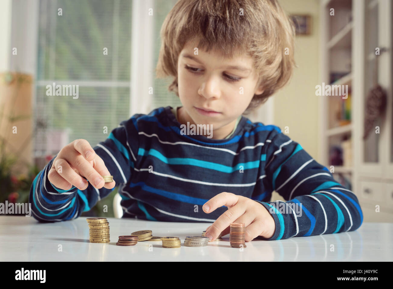Kleiner Junge spielt mit Münzen machen Stapel. Lernen Finanncial Verantwortung und Planung Einsparungen Konzept. Stockfoto
