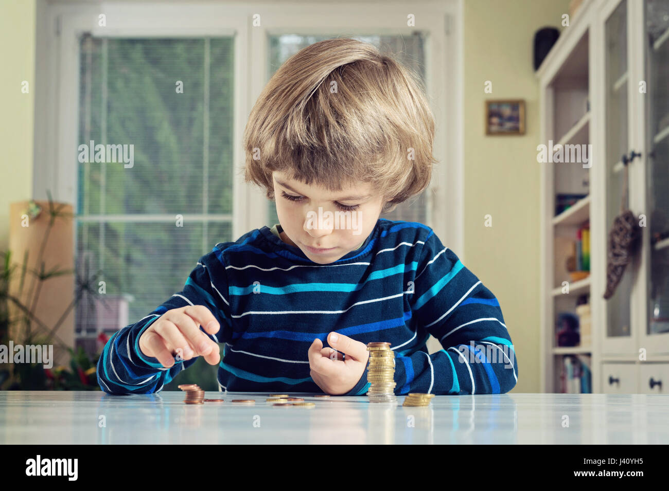 Kleiner Junge spielt mit Münzen machen Stapel. Finanzielle Verantwortung lernen und Planung Einsparungen Konzept. Stockfoto