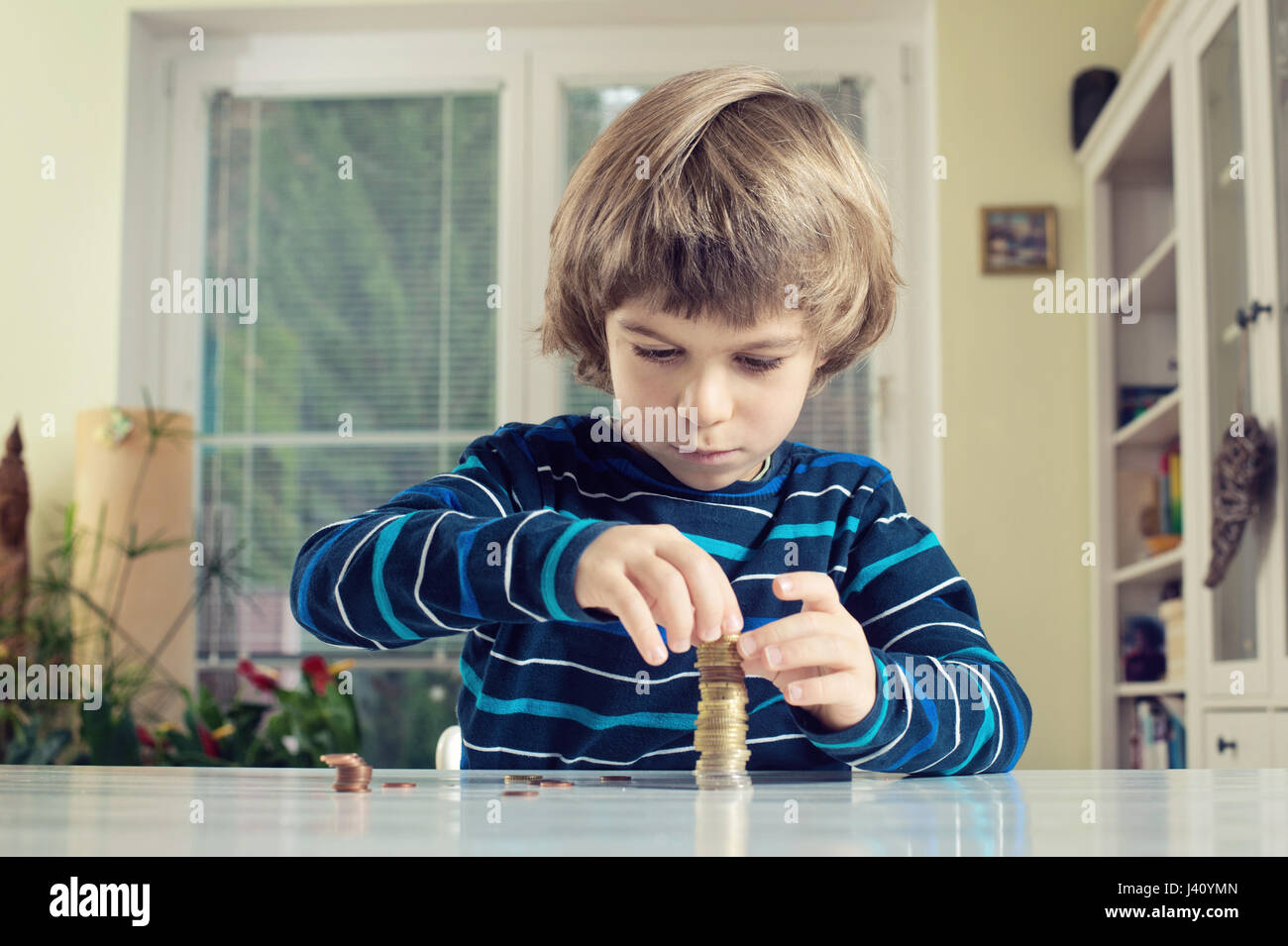 Kleiner Junge macht Stapel von Münzen, Geld am Tisch zu zählen. Finanzielle Verantwortung lernen und Planung Einsparungen Konzept. Stockfoto