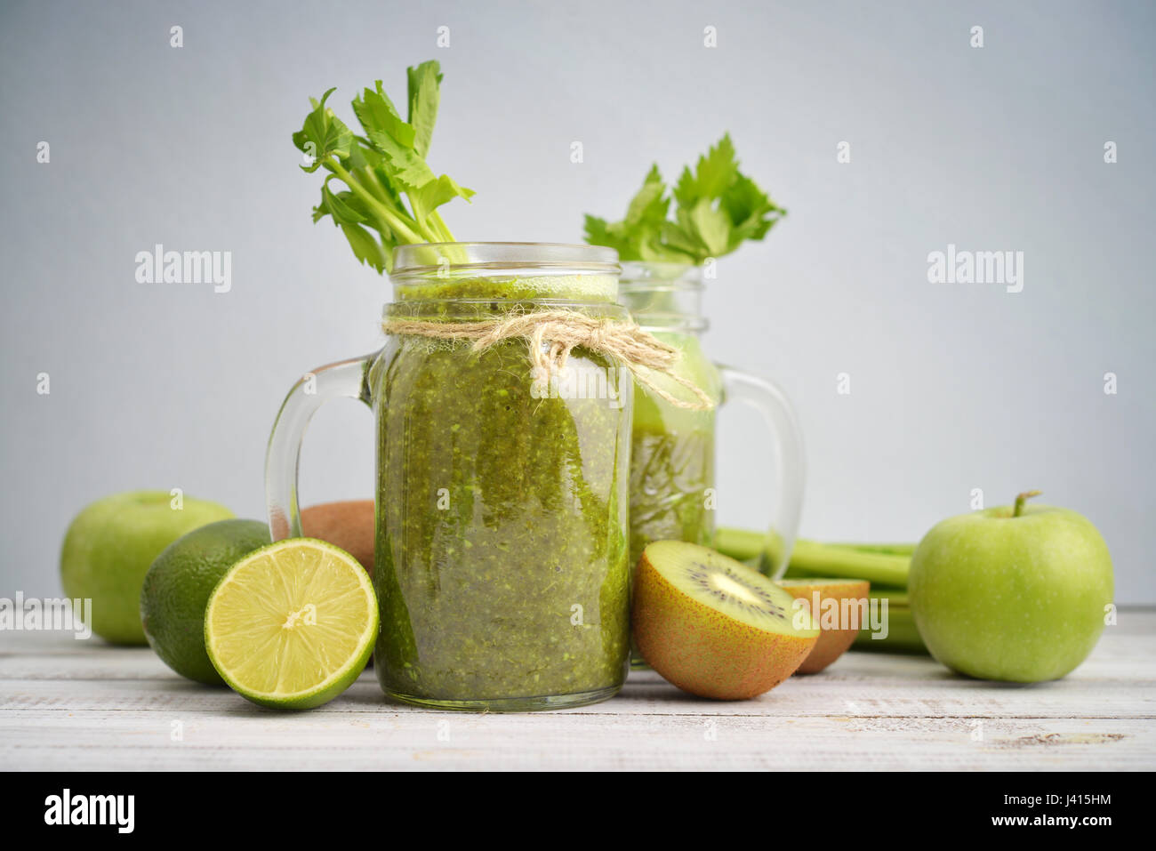 Grüner Smoothie mit Sellerie, Kiwi, Spinat, Apfel und Limette in Gläsern mit Griffen auf blauem Hintergrund Stockfoto