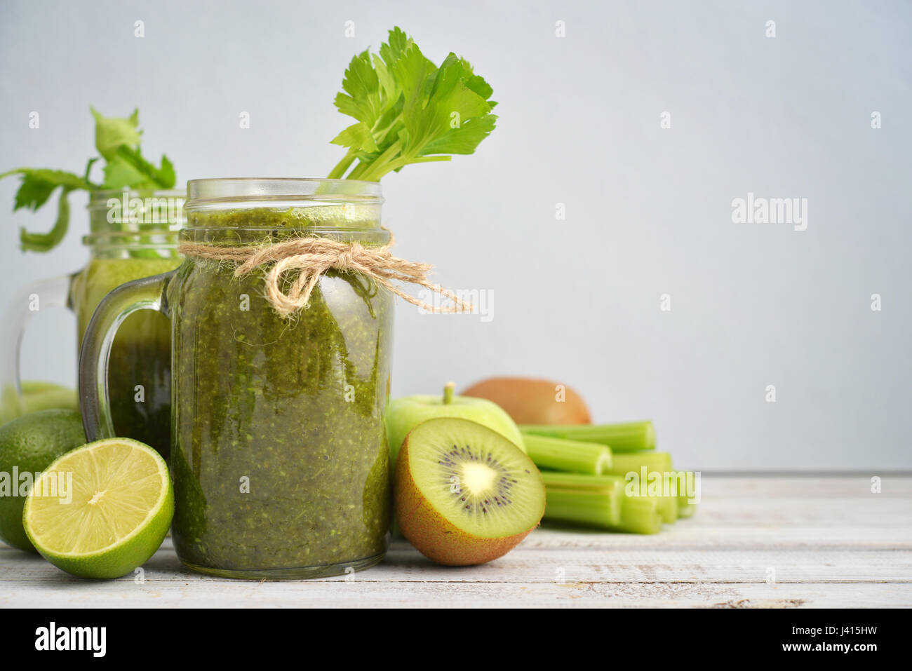 Grüner Smoothie mit Sellerie, Kiwi, Spinat, Apfel und Limette in Gläsern mit Griffen auf blauem Hintergrund Stockfoto